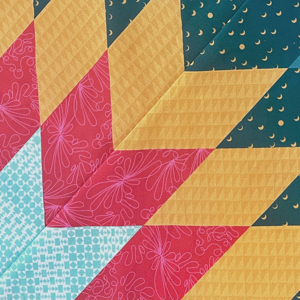 Close-up of Lone Star quilt diamonds in red, teal, aqua and mustard prints meeting at a star point