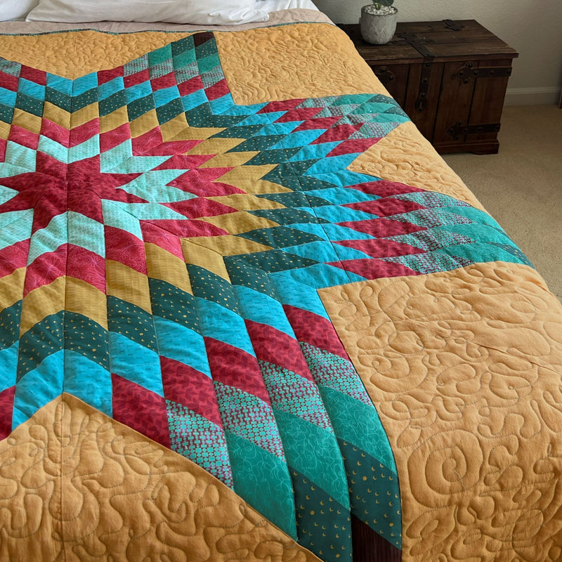 Lone Star quilt with a red, teal and turquoise star on a mustard background, quilted and laid on a bed