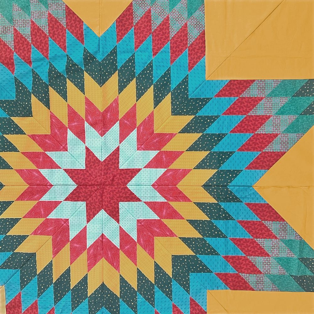 Lone Star quilt top laid flat, an eight-point star of red, teal and aqua diamonds on a mustard background