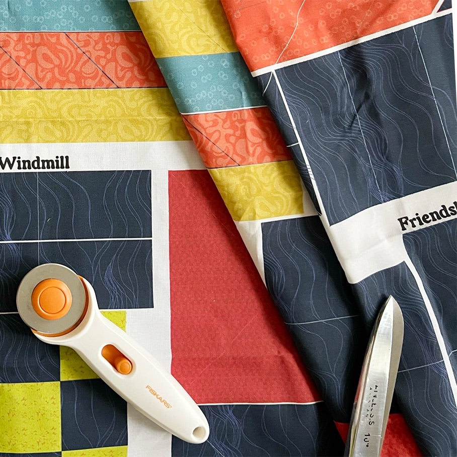 Printed Midnight Stars fabric panel with its cutting lines, beside a rotary cutter and scissors