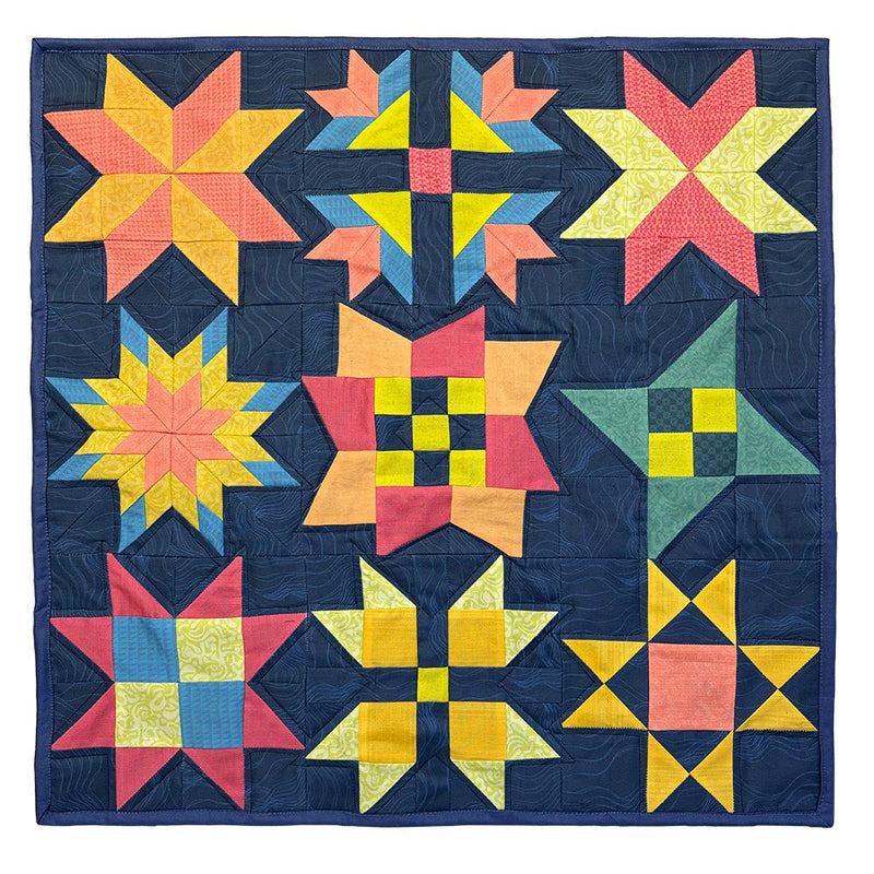 A square quilt featuring nine colorful geometric star and sawtooth star block patterns arranged in a grid on a dark navy blue background. The quilt includes bright yellow, orange, pink, green, and blue fabrics with visible quilting lines. Ohio star and lone star