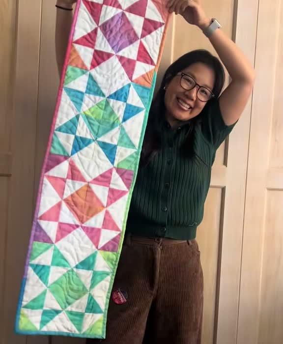 Women proudly holding quilted table runner with ohio star pattern in rainbow colors